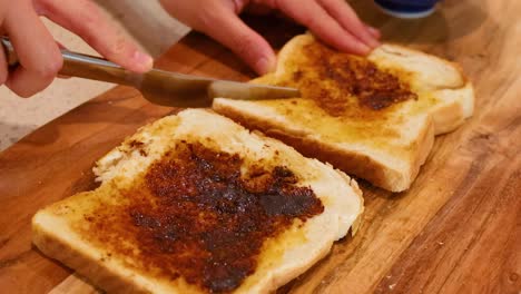 close-up of hands using a knife to spread a dark spread on toasted bread slices on a wooden board.