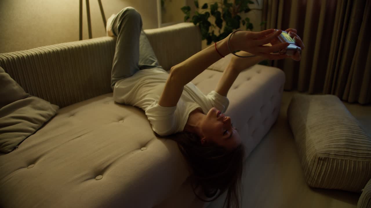 소파에 위아래로 누워있는 여자가 플레어와 함께 사진 카메라를 사용하고 있습니다.