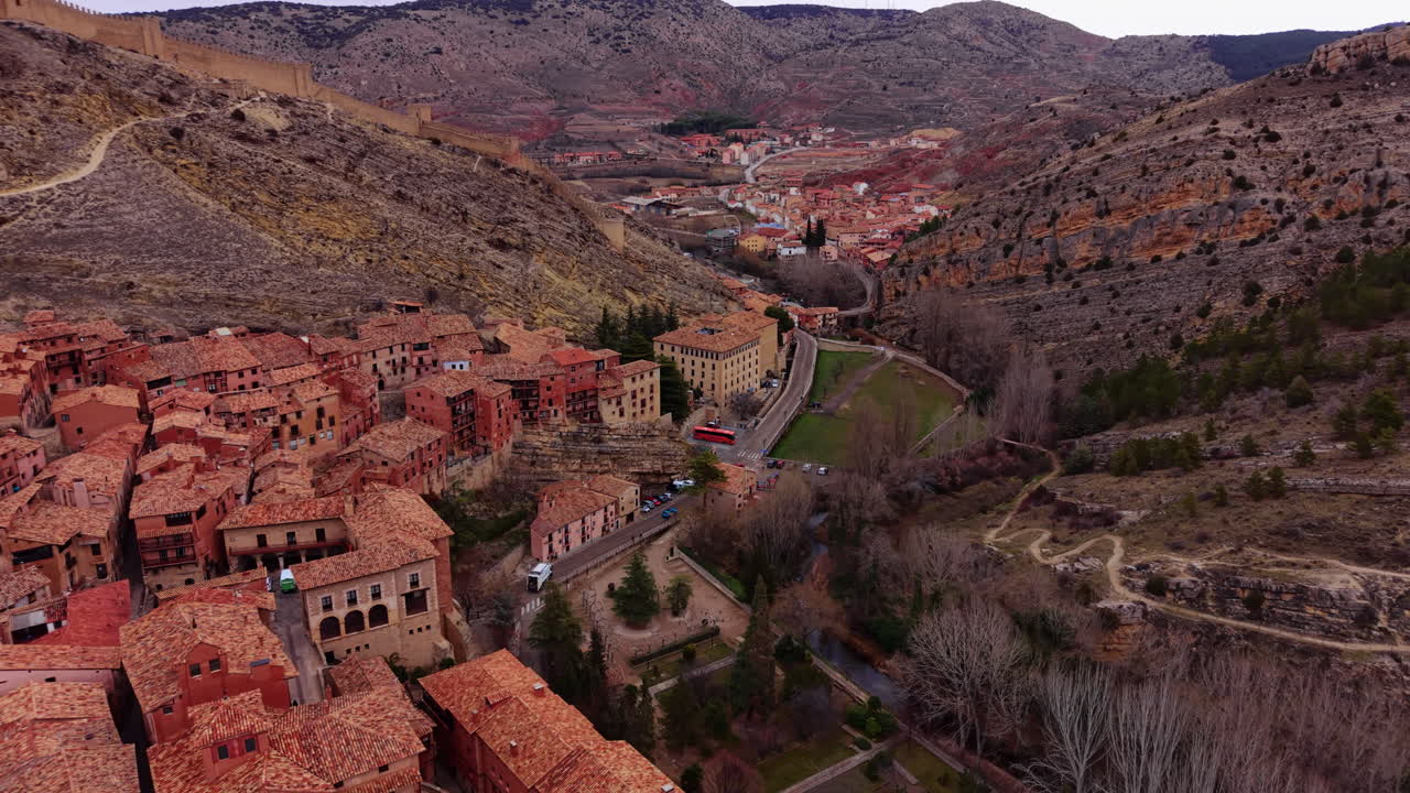 Vista aerea di Albarracín, Teruel, con mura medievali, tetti in terracotta densi e torre della chiesa con tegole colorate incastonata in un aspro paesaggio canyon.