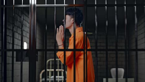 side view of asian male prisoner in handcuffs standing in prison, making pray hand gesture asking for something