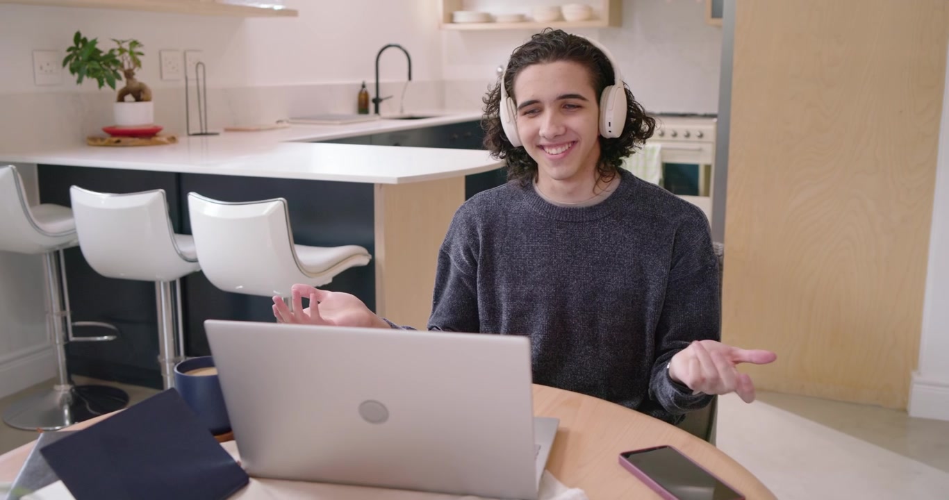 Homem afro-americano ouvindo um aviso, falando e gesticulando para o laptop na cozinha para uma reunião remota