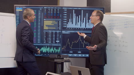 men in suits in room with big digital screen with data