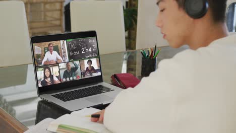 asian teenage boy using laptop for video call, with male teacher and class on screen