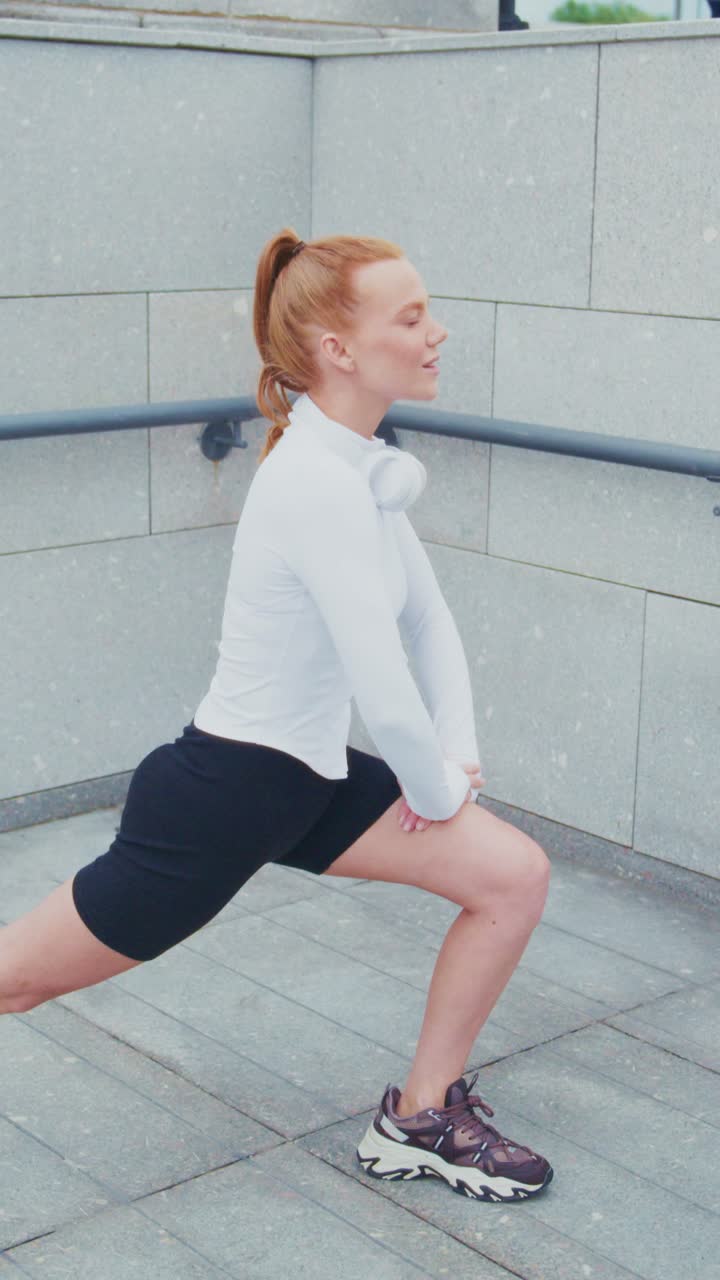 A Young Woman Engaging in a Lunge Exercise Outdoors, Demonstrating Proper Form and Fitness Apparel While Wearing Headphones for an Enhanced Workout Experience