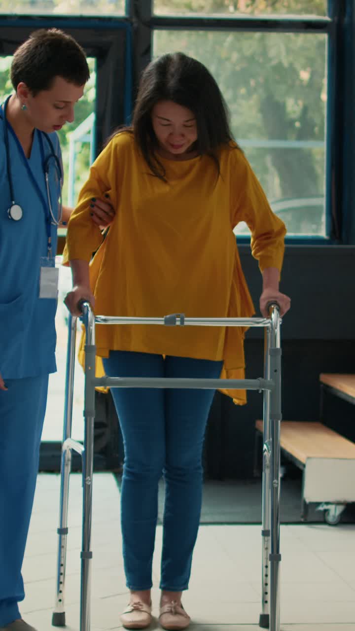 Vertical video: Female nurse helping patient with leg injury to use walk frame