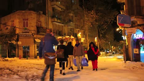 people walk through unusually snowy streets past noya restaurant in jerusalem at night