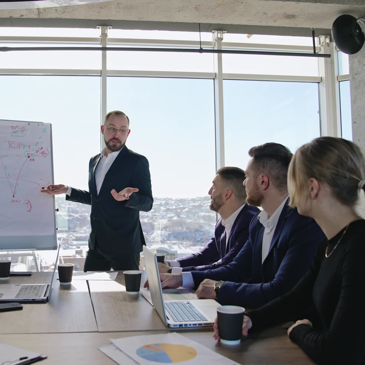 Male speaker communicating with his coworkers at office. Business meeting for planning and building strategies at work. City view at backdrop