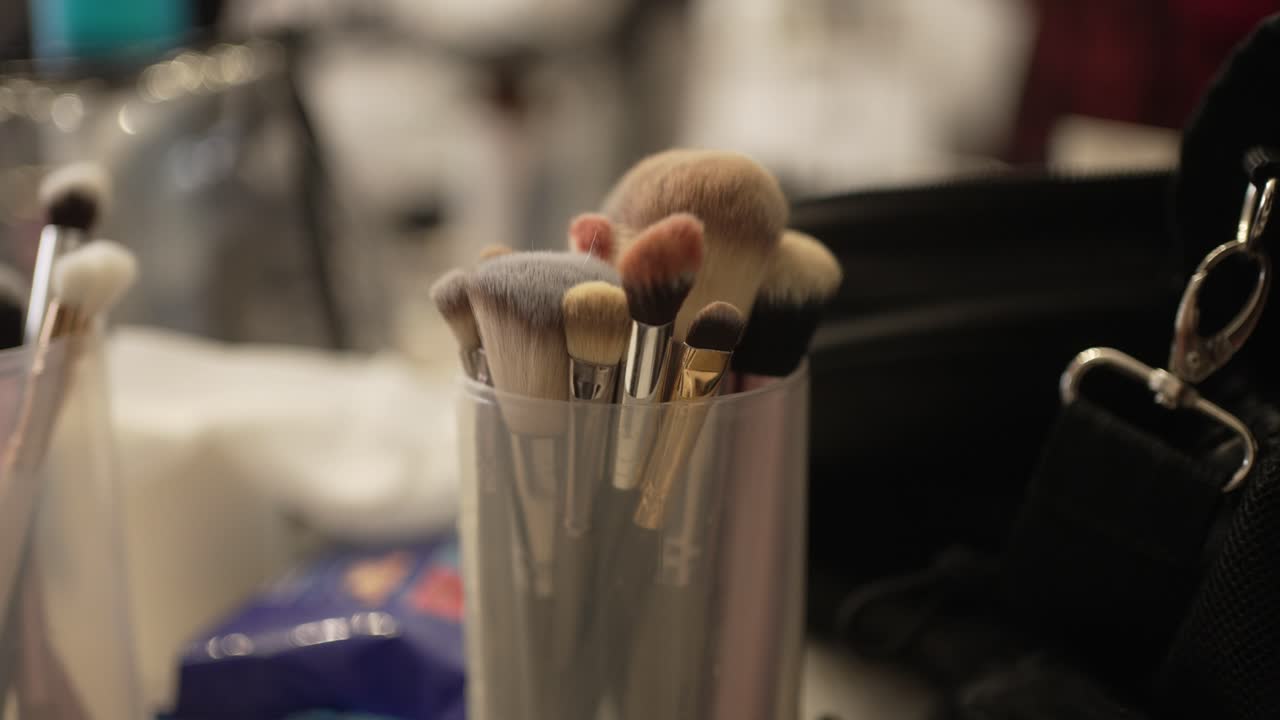 Close up of assorted makeup brushes inside a plastic cup on a dressing table with blurred background