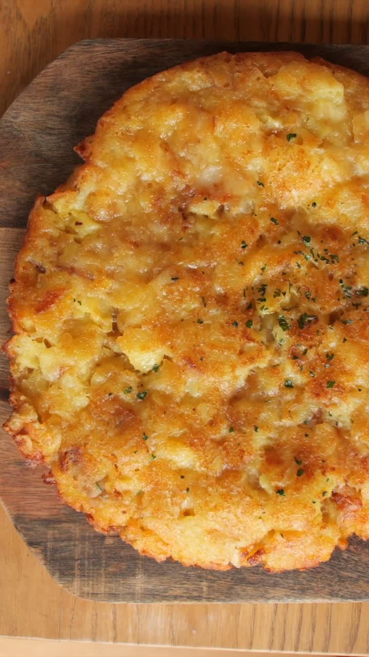 Ripresa verticale e roteante dall'alto di una frittata di formaggio, patate e uova, su piatto di legno decorato.