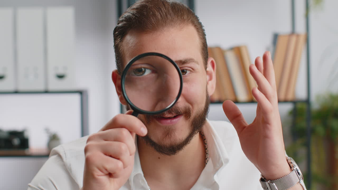 Business man holding magnifying glass near face looking with big zoomed eye searching analysing