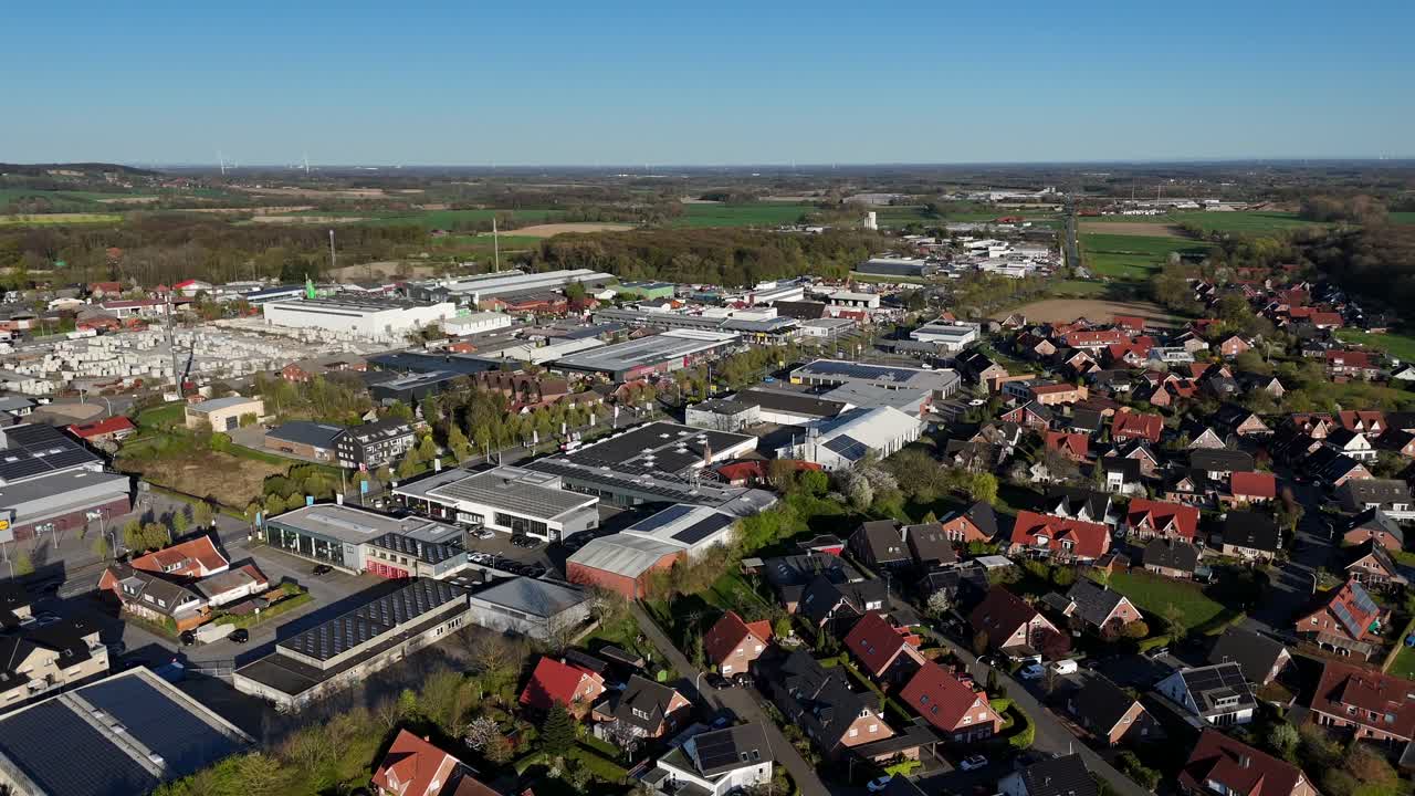 industrial district with warehouses and solar panels on roof. Bordering to american housing area with single family houses at sunset. Colored farm fields in distance. Aerial lateral wide shot.