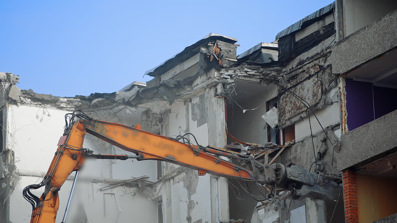 Ruins of the building under blue sky being demolished by the excavator machine. Disrupted house under the process of demolition for future city development.