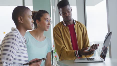 Diverse-male-and-female-creative-colleagues-in-discussion-standing-together-at-laptop