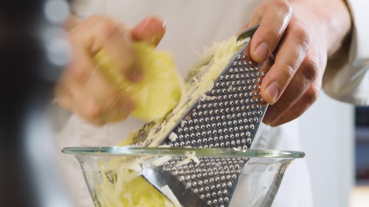Hand of chef grating potatoes in glass bowl. Handheld shot and close up