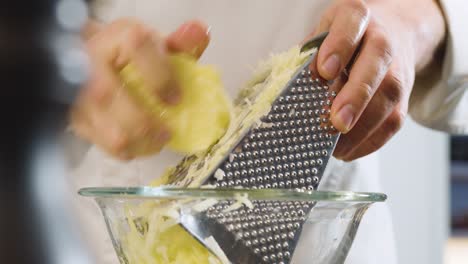 hand of chef grating potatoes in glass bowl. handheld shot and close up