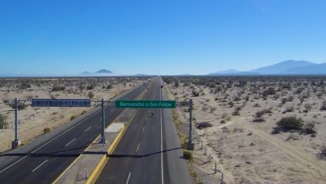 view of a drone flying back over a sign on a highway that says "bienvenidos a san felipe