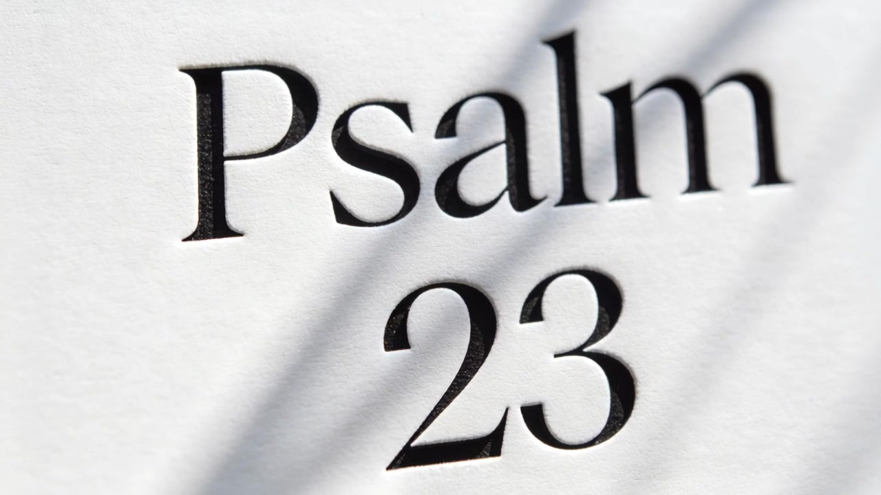 Shifting light casting soft shadow across printed serif Psalm 23, revealing imprint and focus shift