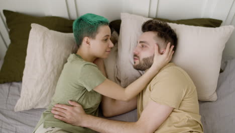 top view of a loving couple talking and looking at each other while lying on the bed