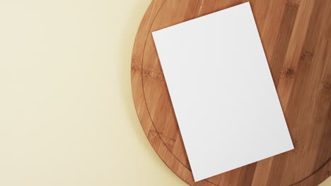 Video-of-book-with-white-blank-pages-and-copy-space-on-wooden-chopping-board-and-yellow-background