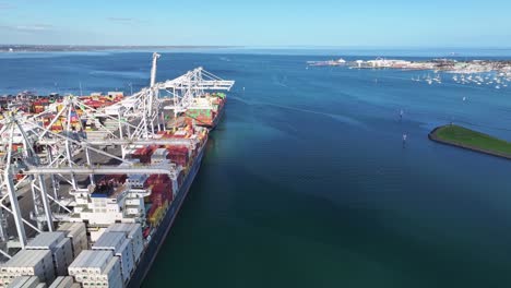 container ship docked beside cranes and colourful containers at melbourne maritime freight terminal