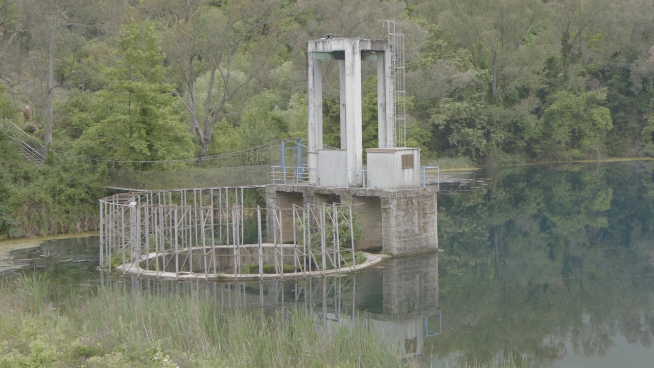 Stará betonová vodní odběrná věž a přeliv na jezeře Blue Eye Reservoir v Albánii.