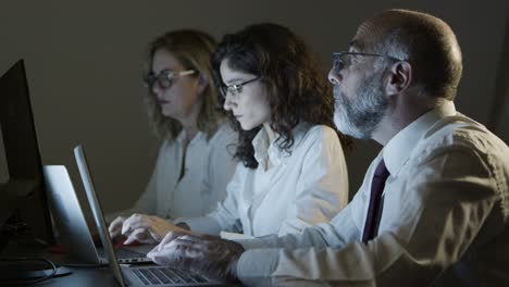 compañeros de trabajo sobrecargados de trabajo usando computadoras portátiles en la oficina oscura