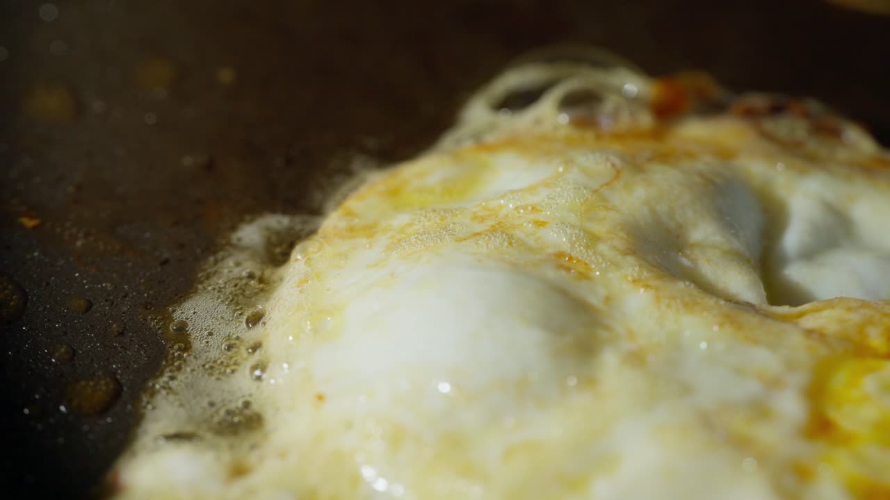Fried easy over egg cooking on sizzling hot surface with foaming butter, macro