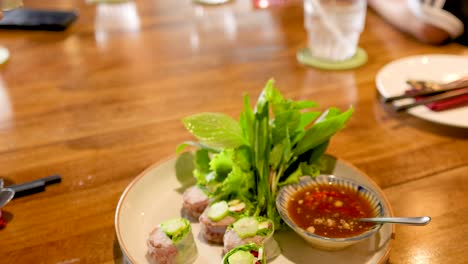 hands preparing and dipping vietnamese pork rolls in sauce at a bangkok restaurant. bright lighting enhances the vibrant, fresh ingredients