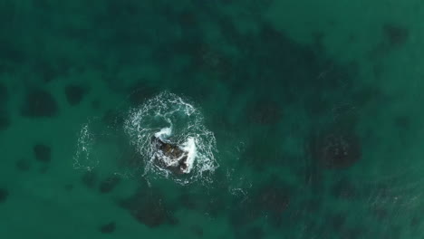 Vista-Superior-De-Drones-De-4k-De-Olas-Rompiendo-En-Una-Roca-Solitaria-En-Un-Mar-Azul