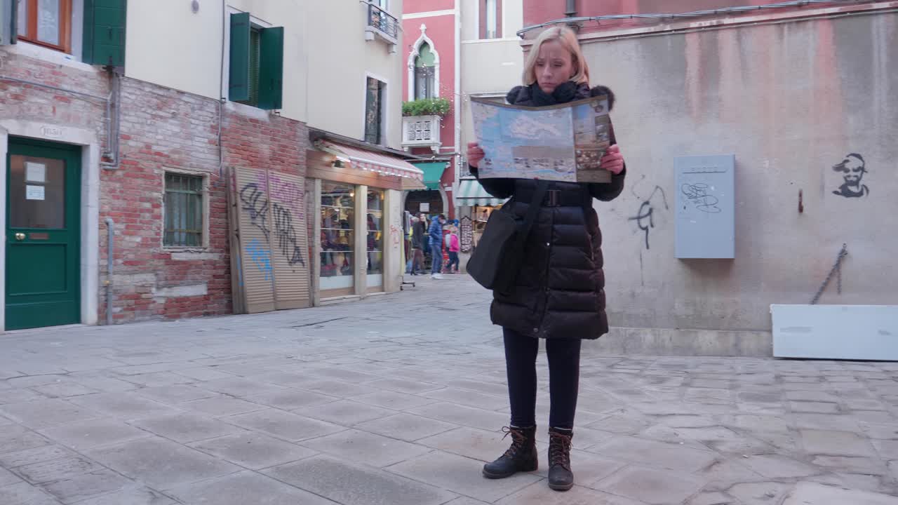 Donna in un vicolo che osserva una mappa e controlla i dintorni per orientarsi a Venezia, Italia