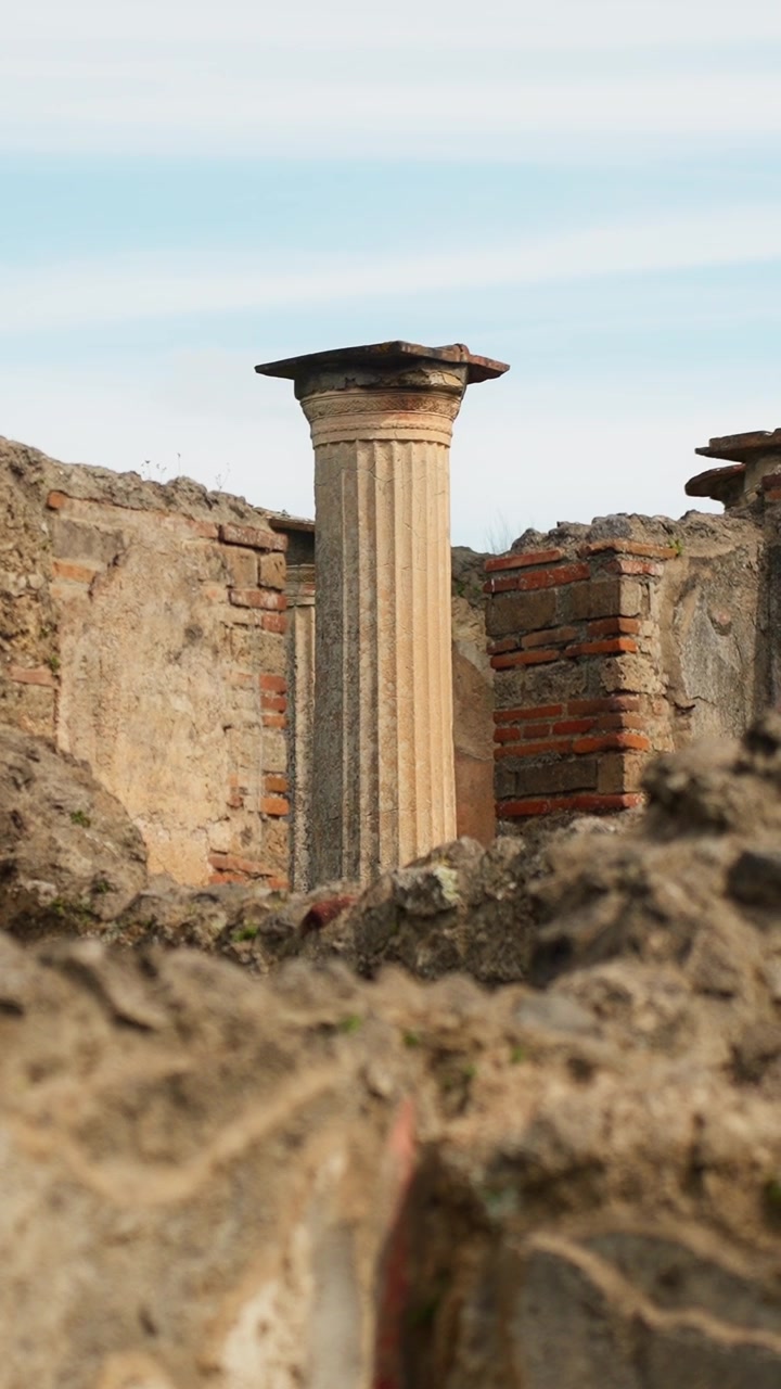 Vertical close-up of a surviving fluted column in Pompeii, framed by rough foreground stones and ruined walls inside the ancient Roman archaeological site.