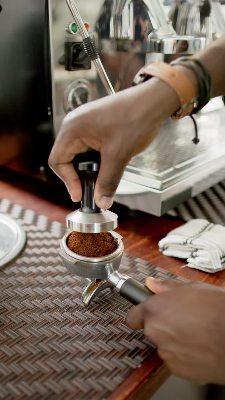 Vertical video: Preparing espresso, barista tamping coffee grounds in portafilter at cafe