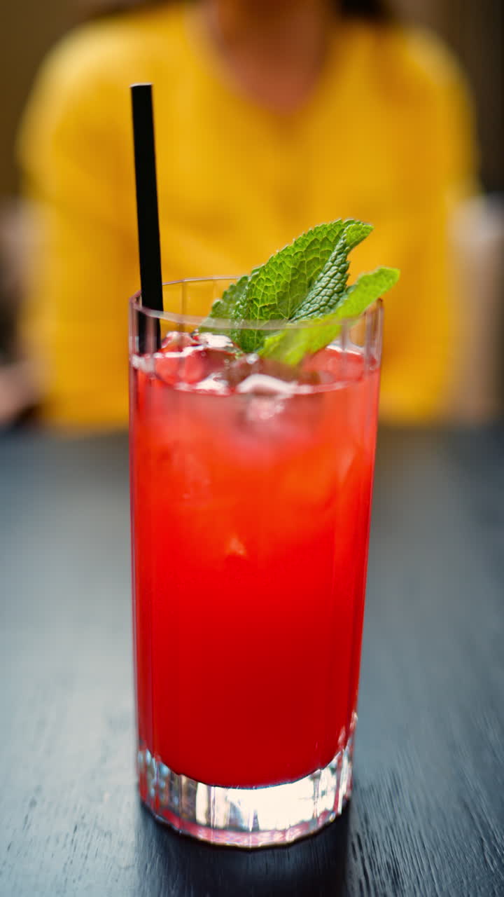 A red drink with ice and mint in a transparent glass at a cafe. Vertical