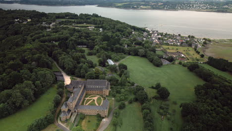 Panorama-Dolly-Luftaufnahme-Eines-Großen-Klostergebäudes,-Umgeben-Von-Bäumen-Bergauf,-Einem-Dorf-An-Einem-Fluss