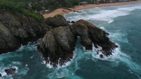 Aerial-orbit-shot-of-a-big-rock-formation-with-Zipolite-beach-behind,-Oaxaca