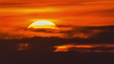 View-of-yellow-sun-setting-in-the-orange-sky-with-dark-clouds-passing-by-in-timelapse