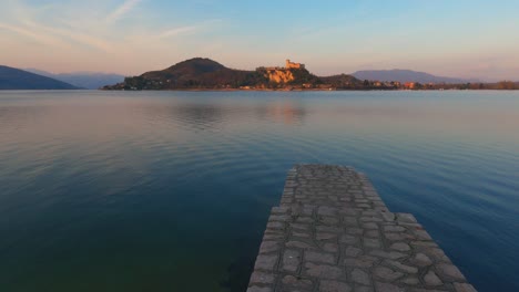 Escena-Pacífica-Del-Muelle-De-Hormigón-En-El-Lago-Maggiore-Aguas-Tranquilas-En-Italia,-Castillo-De-Angrya-En-El-Fondo