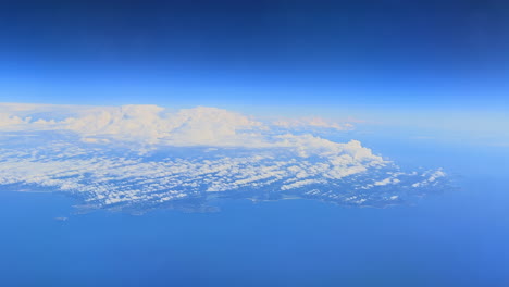 Airplane-view-of-coast-of-Spain-below-white-clouds-and-bright-blue-sky