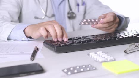 Médico-Escribiendo-En-El-Teclado-De-La-Computadora-Sosteniendo-Pastillas-Medicinales,-Cita-De-Nutrición,-Primer-Plano