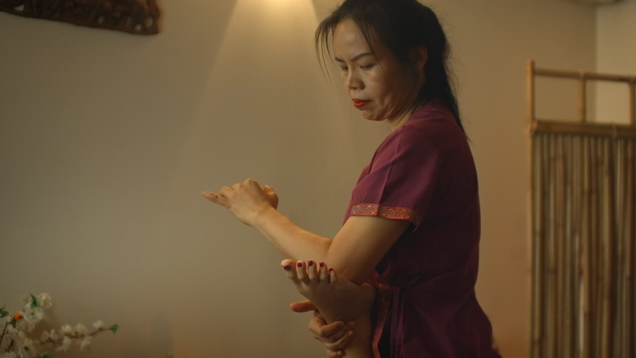 Alternative Chinese medicine an Asian woman performs therapeutic massage on the back and legs of a Caucasian woman lying on a couch. Aromatherapy and manual therapy by Chinese masters.