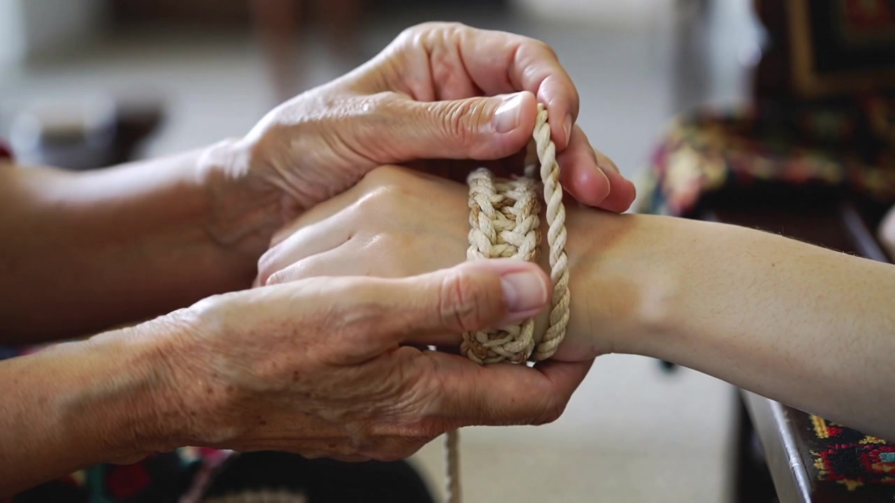 Holding adult wrist, senior hands fastening braided band and looping rope at home, patterned sleeve