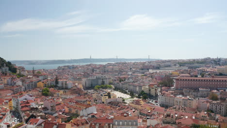 Drone-camera-flying-over-red-tiled-roof.-Wide-city-panorama-reveals-behind-roof-ridge.-Lisbon,-capital-of-Portugal.