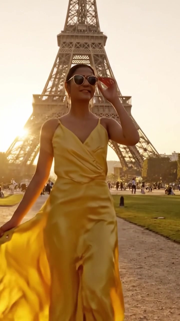 Una donna elegante in un abito giallo svolazzante passeggia verso l'iconica torre al tramonto, catturando l'essenza dell'eleganza e del fascino parigino in una scena incantevole.