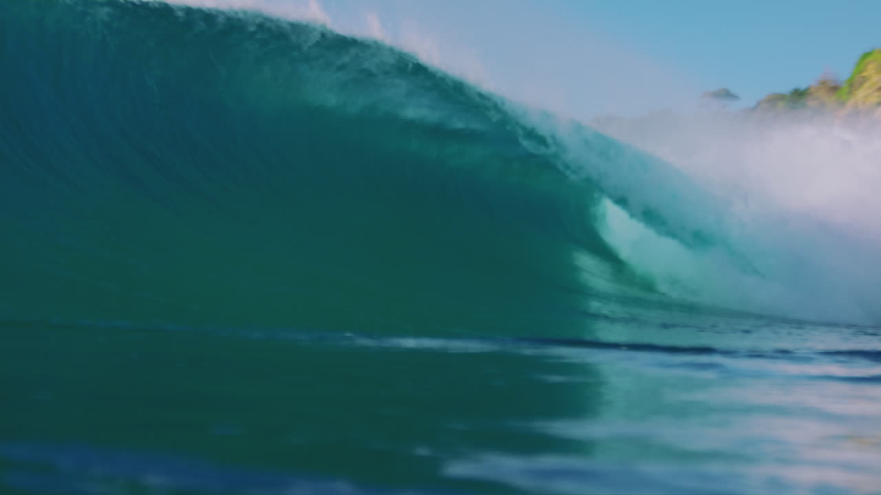 Slow-motion view of a large wave curling over into a perfect barrel, filmed from outside the water during sunrise, showcasing the wave's power and shape
