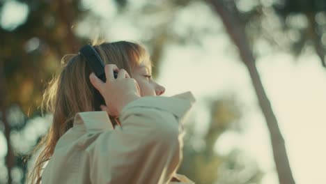 Girl-puts-headphones-on-head-at-golden-hour,-listens-to-podcast