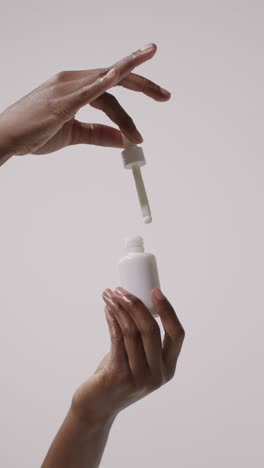 close up of woman holding bottle of beauty product and dropper on white background