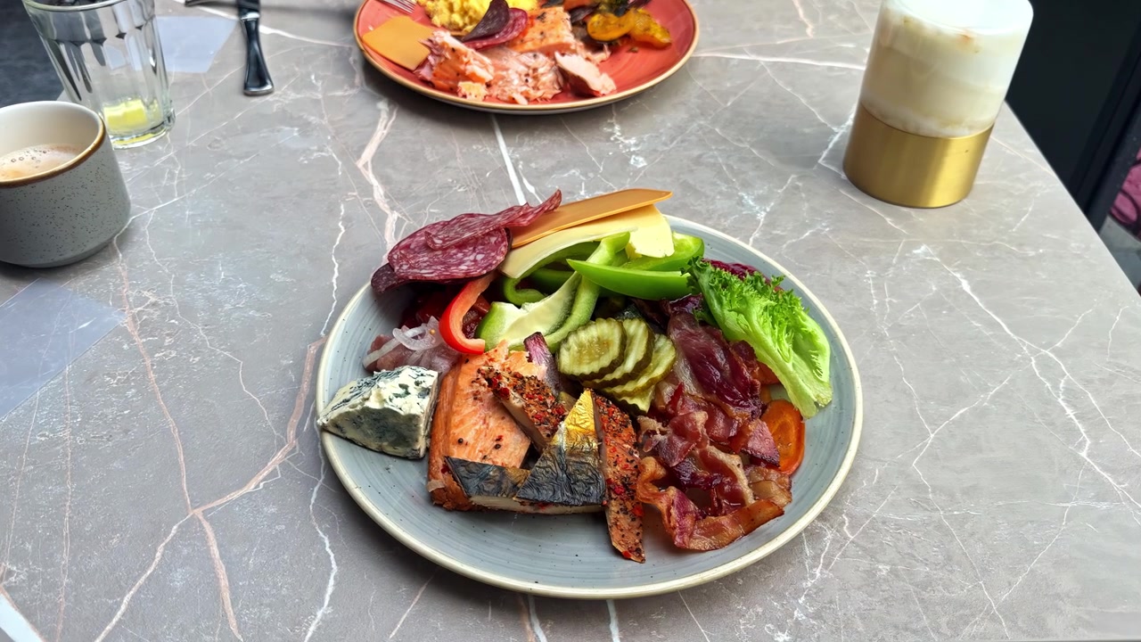 La telecamera si avvicina lentamente a un abbondante piatto per la colazione con salmone grigliato, pancetta, salame, formaggio e verdure