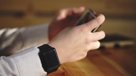 person using smartphone and smartwatch at a wooden table