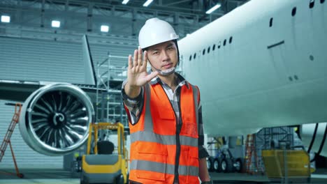 ingeniero masculino asiático con casco de seguridad desaprueba sin señal de mano mientras está de pie con la aeronave en el hangar