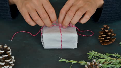 woman hands tie the red rope of a gift box with white wrapping